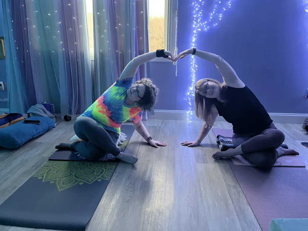 Two students making a heart shape in a seated side stretch